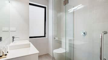 Un baño moderno con cabina de ducha de vidrio, lavabo blanco y retrete.