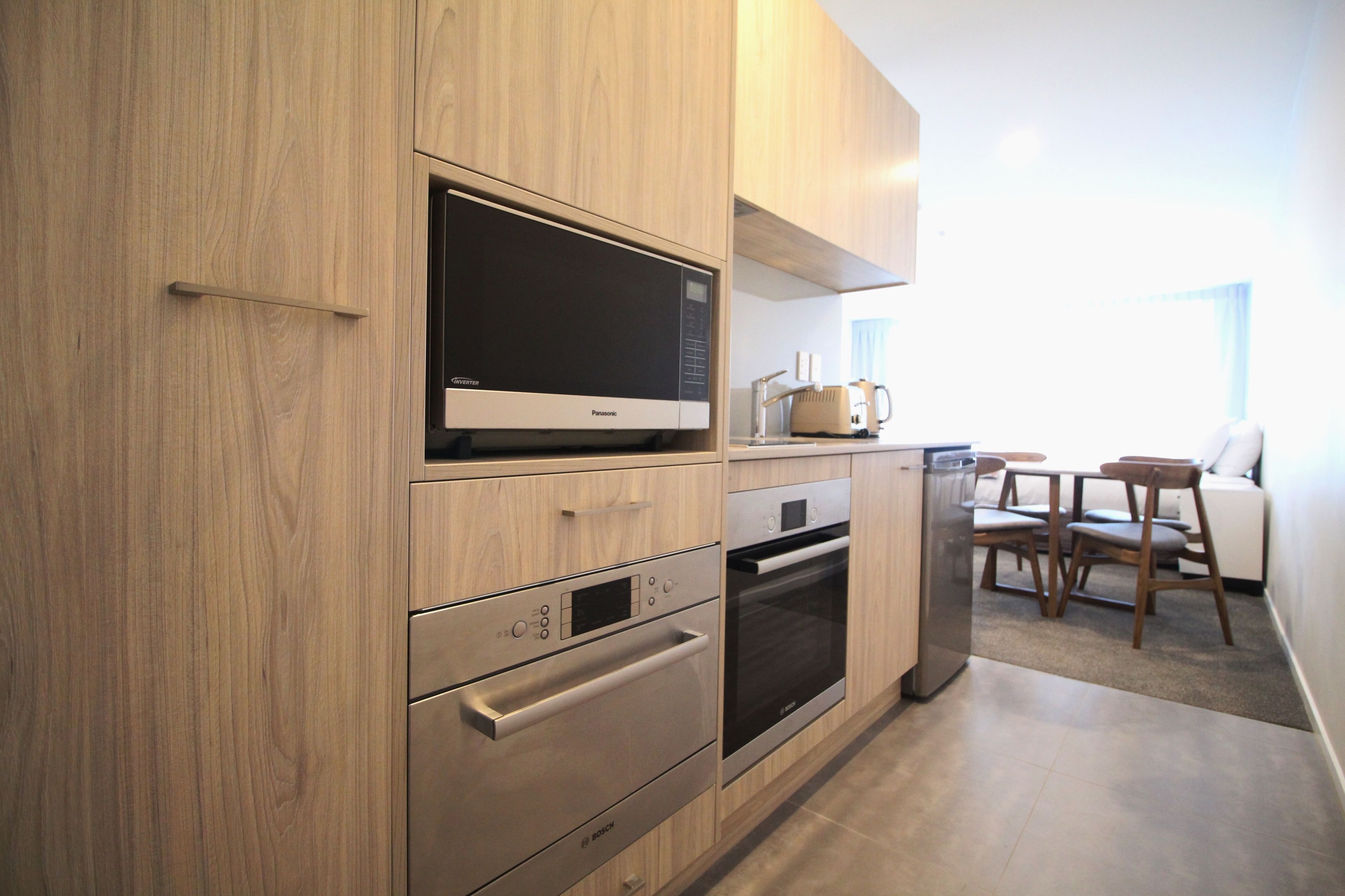 A modern kitchen with built-in appliances, a dining area with a table and chairs, and a view of the outdoors.