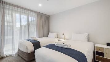 Habitación de hotel con dos camas, una mesita de noche con lámpara, un armario y un atril.