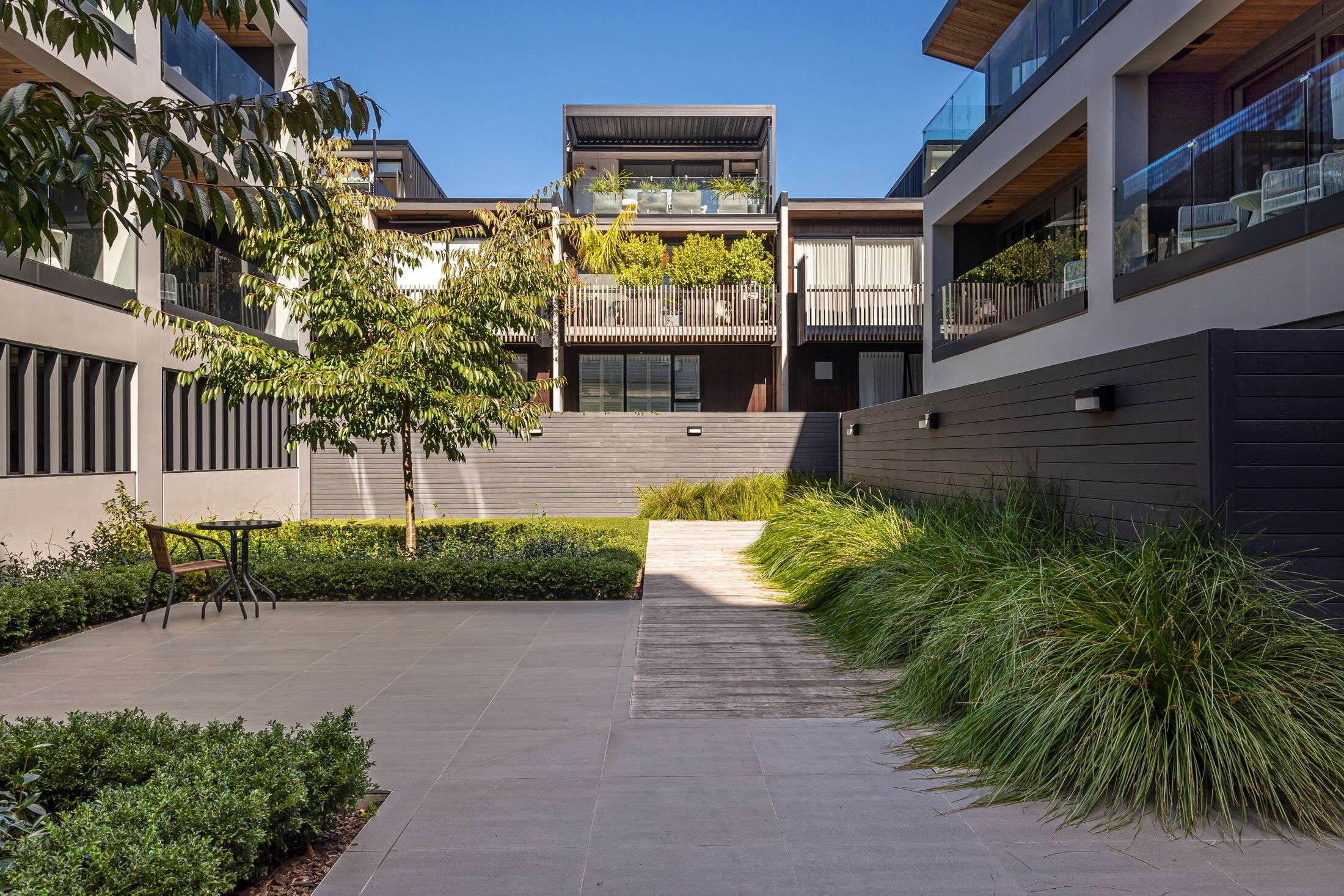 A modern building with a courtyard featuring a seating area, a pathway, and lush greenery.