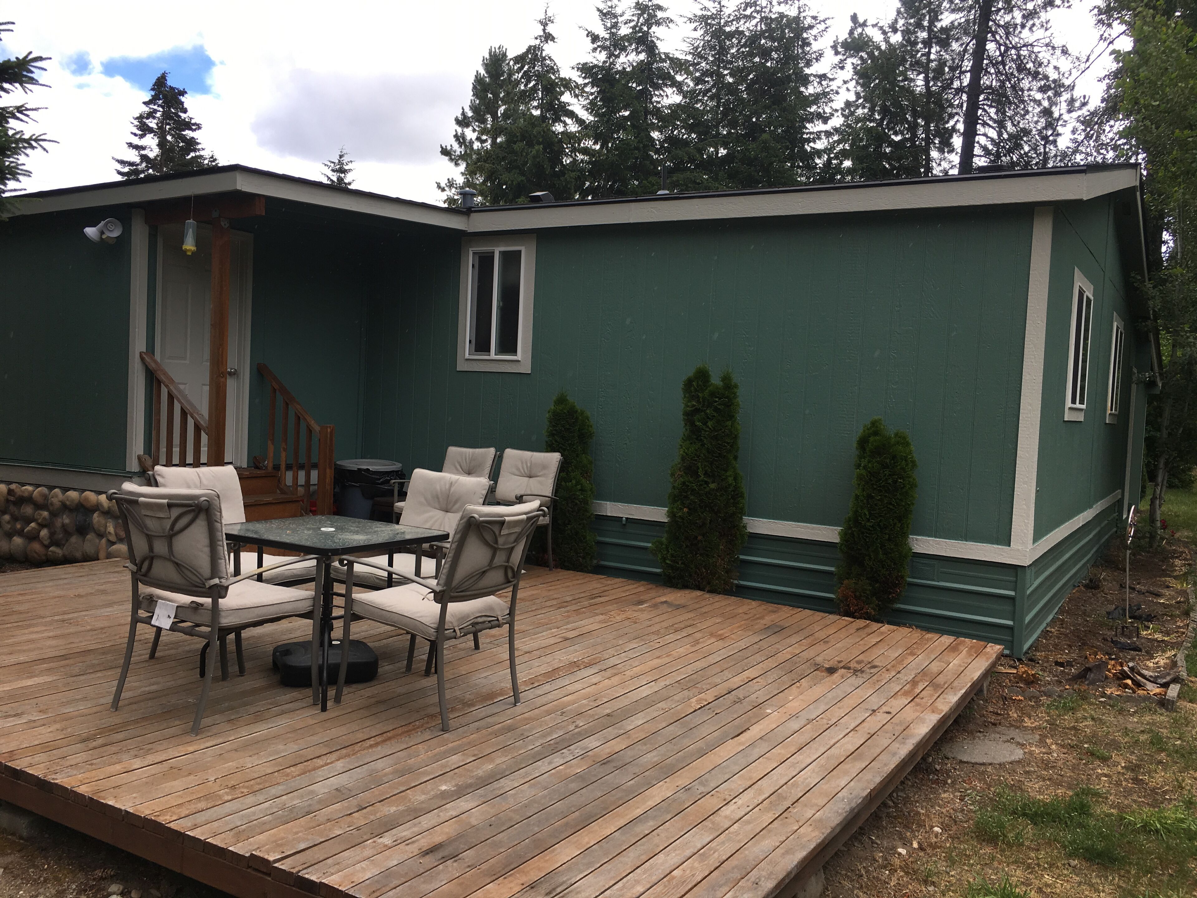A green house with a wooden deck, outdoor seating, and a staircase leading to the entrance.