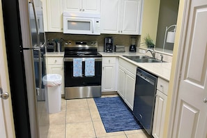 A compact kitchen with white cabinets, stainless steel appliances, and a blue rug.