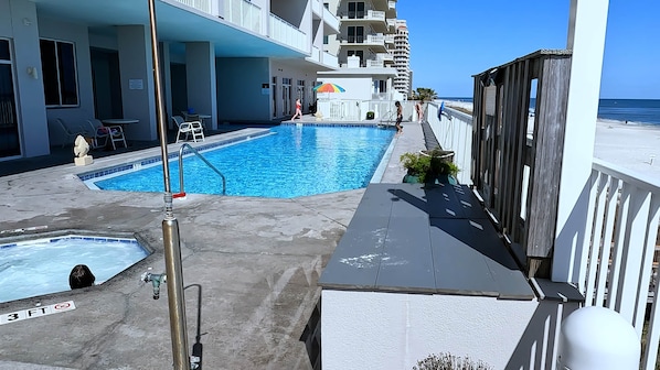 A swimming pool area with a small pool and a larger pool, surrounded by a building with balconies and a view of the beach.