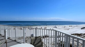 A beach with a white fence, a view of the ocean, and people on the sand.
