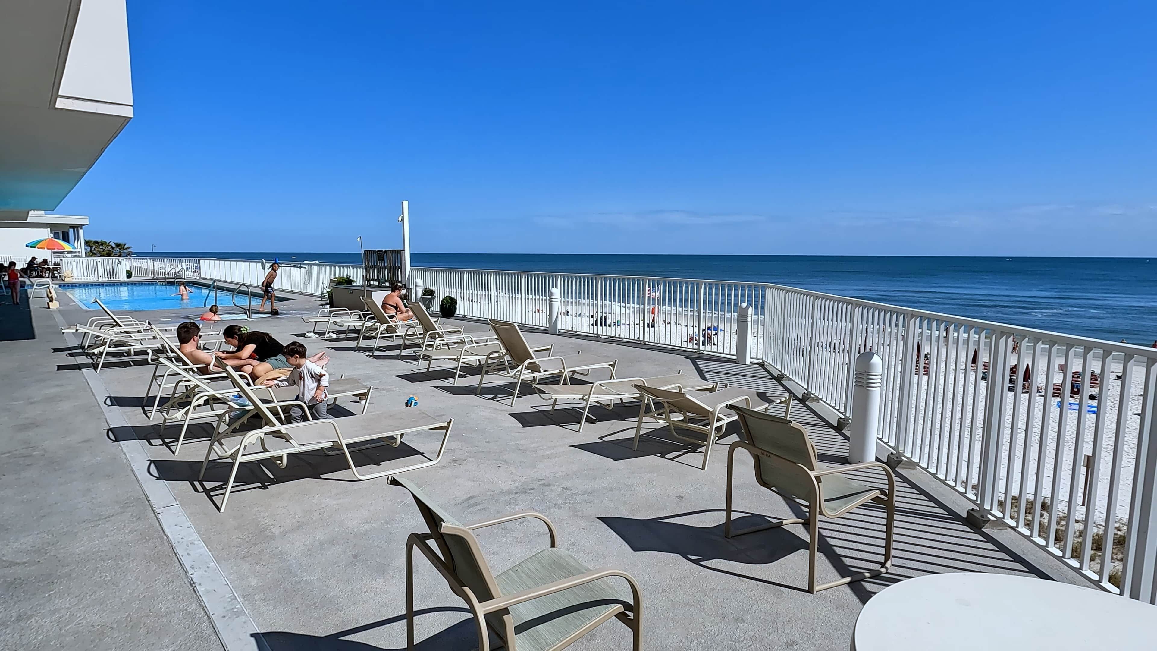 A poolside area with lounge chairs and a view of the ocean.