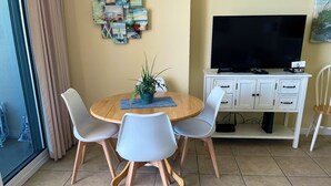 A dining area with a round table, four chairs, a potted plant, a flat-screen TV, a cabinet with drawers, and a wall with artwork. - MILLION DOLLAR VIEW WITH PRIVATE PARKING SLEEPS 6, BOOK 7 DAYS GET 10% DISCOUNT! (Pensacola)