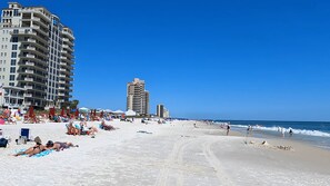 Une plage bordée de nombreux bâtiments d’hôtel, avec un rivage sablonneux et un ciel bleu clair.