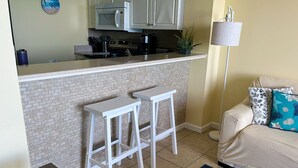 A kitchen with a brick backsplash, two white bar stools, a microwave, and a coffee maker. - MILLION DOLLAR VIEW WITH PRIVATE PARKING SLEEPS 6, BOOK 7 DAYS GET 10% DISCOUNT! (Pensacola)