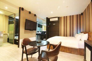 Une chambre d’hôtel comprenant un lit, une télévision, une petite table avec deux chaises, un miroir et une salle de bain visible à travers une porte en verre.