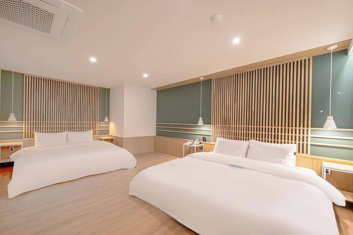 A hotel room with two beds, wooden headboards, bedside tables, and pendant lights.