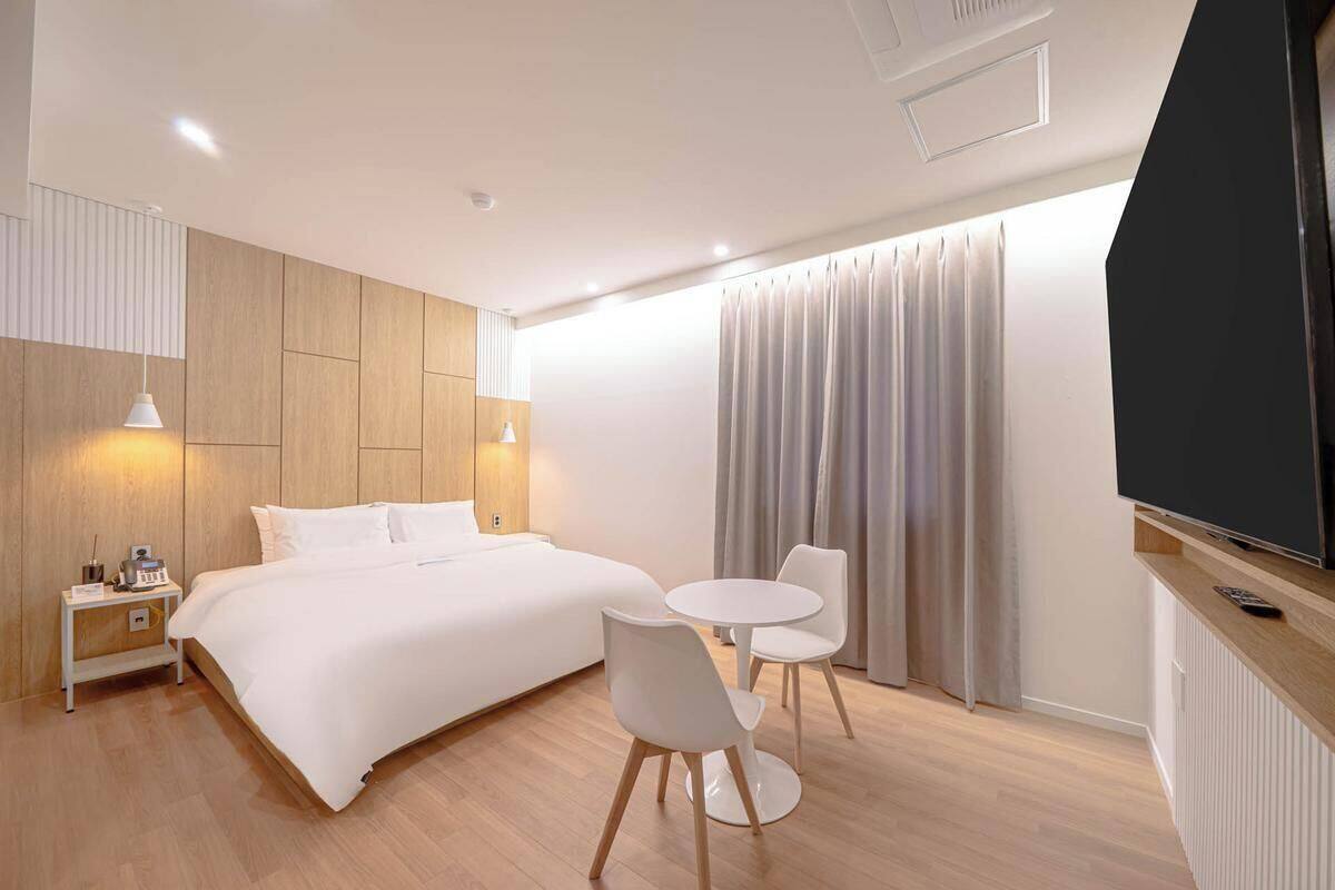 A modern hotel room with a bed, bedside table, lamp, TV, and a small round table with chairs.