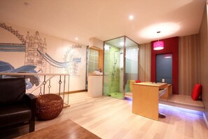 Un salon moderne agrémenté d’une grande fresque murale, d’une douche en verre, d’un bureau en bois et d’un coin salon avec un coussin rouge.