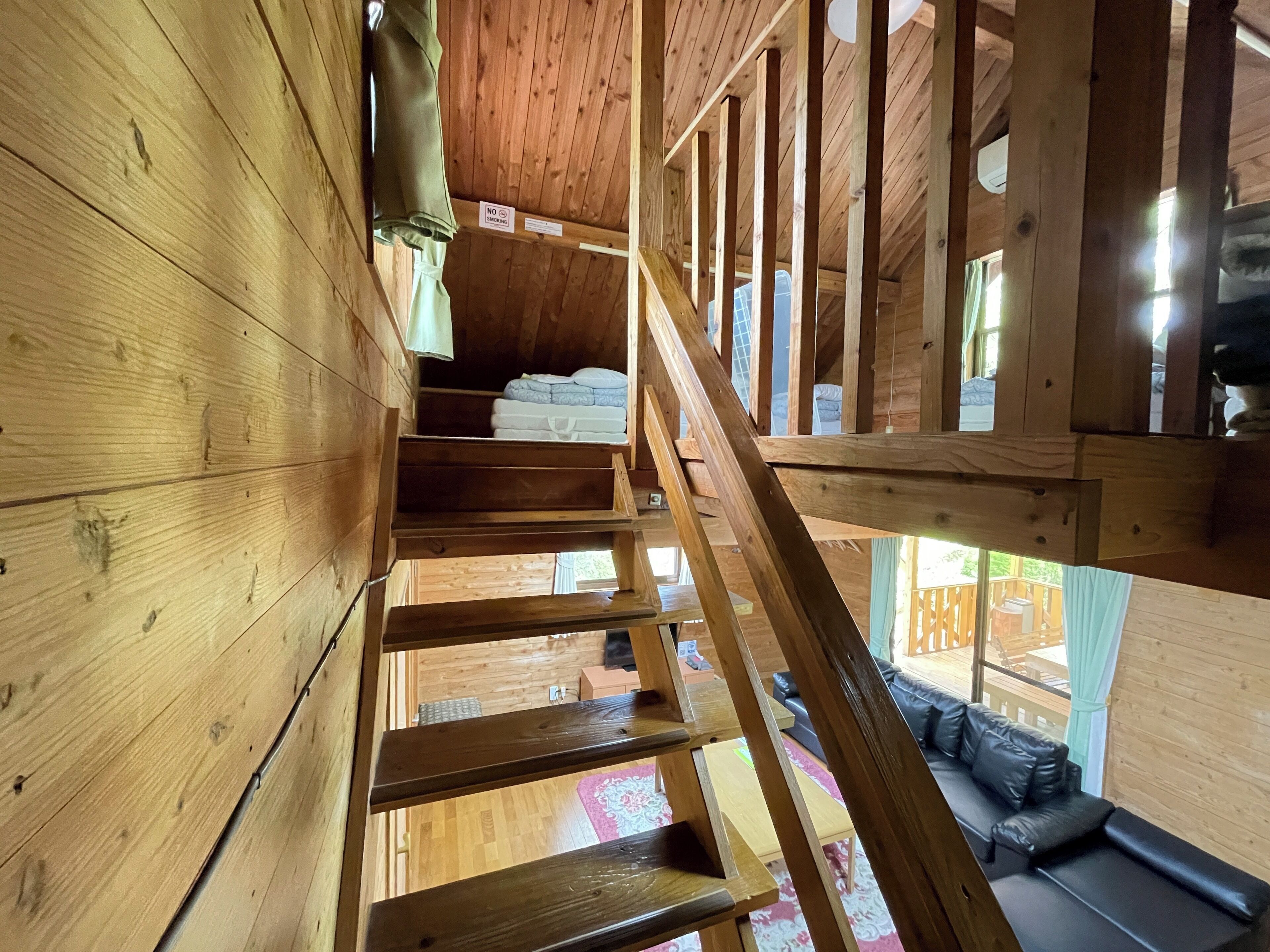 A wooden staircase leading to a loft area with a view of the outdoors.