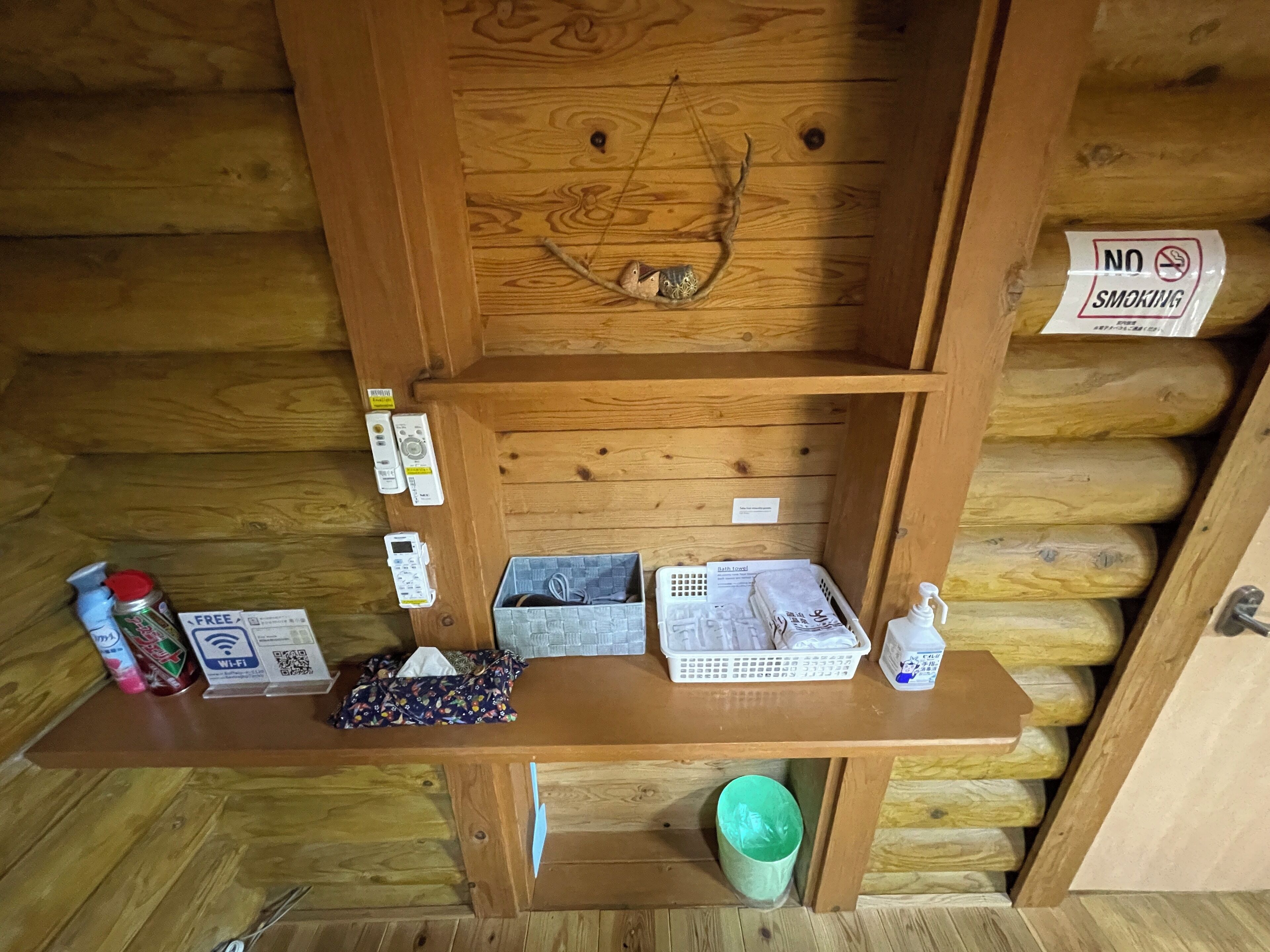 A wooden cabin interior with a shelf containing toiletries, a basket, and a sign indicating no smoking.