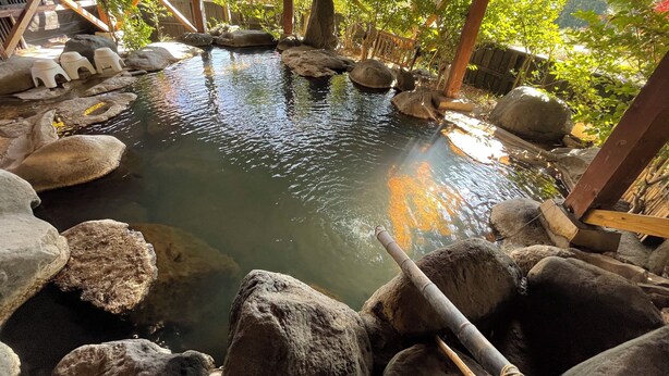 A tranquil outdoor water feature with rocks and a wooden structure. - Kurasako Onsen Sakura (Minamioguni)