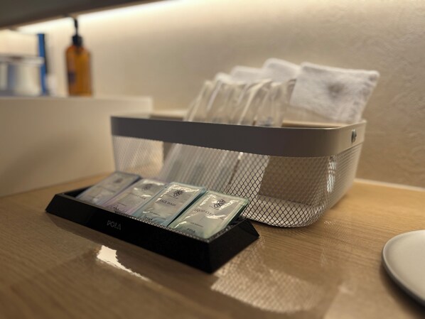 Un espace d’accueil d’hôtel avec un comptoir noir, un panier en treillis contenant des articles de toilette et un petit présentoir avec des produits étiquetés « POLA ».
