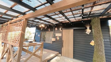 Un espacio al aire libre techado con piso de madera, techo metálico y puerta de madera.