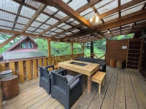 Une terrasse extérieure couverte, dotée d’une table et de chaises en bois, entourée de rampes en bois et agrémentée d’un banc en bois.