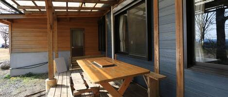 Una terraza de madera con una mesa de picnic y bancos, ventanas grandes y una puerta.