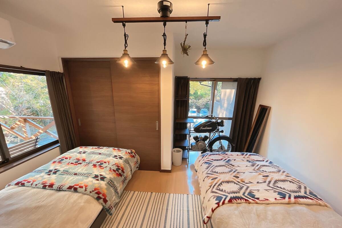 A bedroom with two beds, a wooden wardrobe, a bicycle, and a window with a view of greenery.