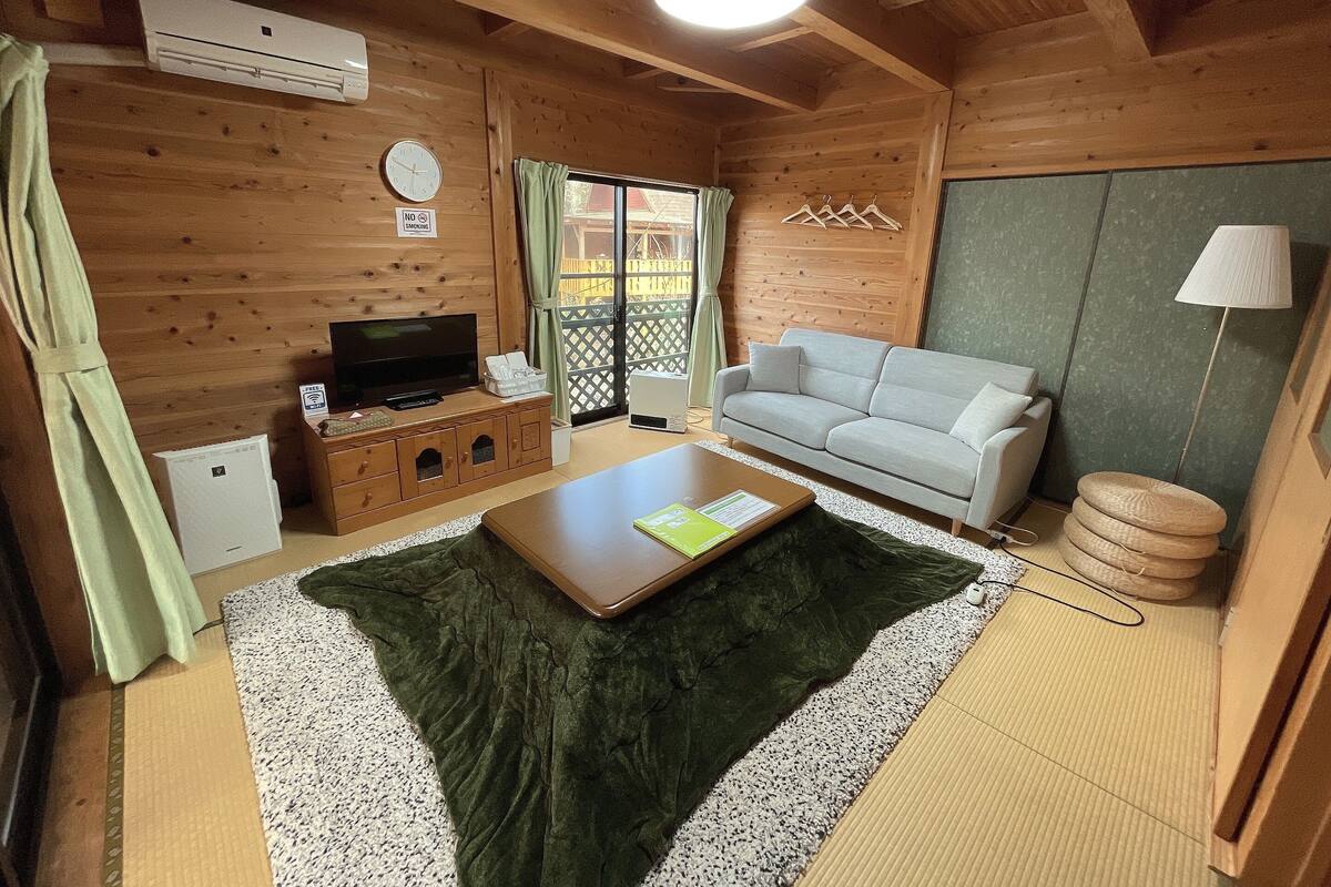 A cozy room with a sofa, a television, a small table, and a window with curtains.