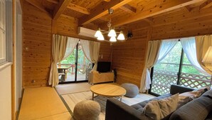 A cozy wooden cabin interior with a sofa, round table, and a television. - Kurasako Onsen Sakura (Minamioguni)