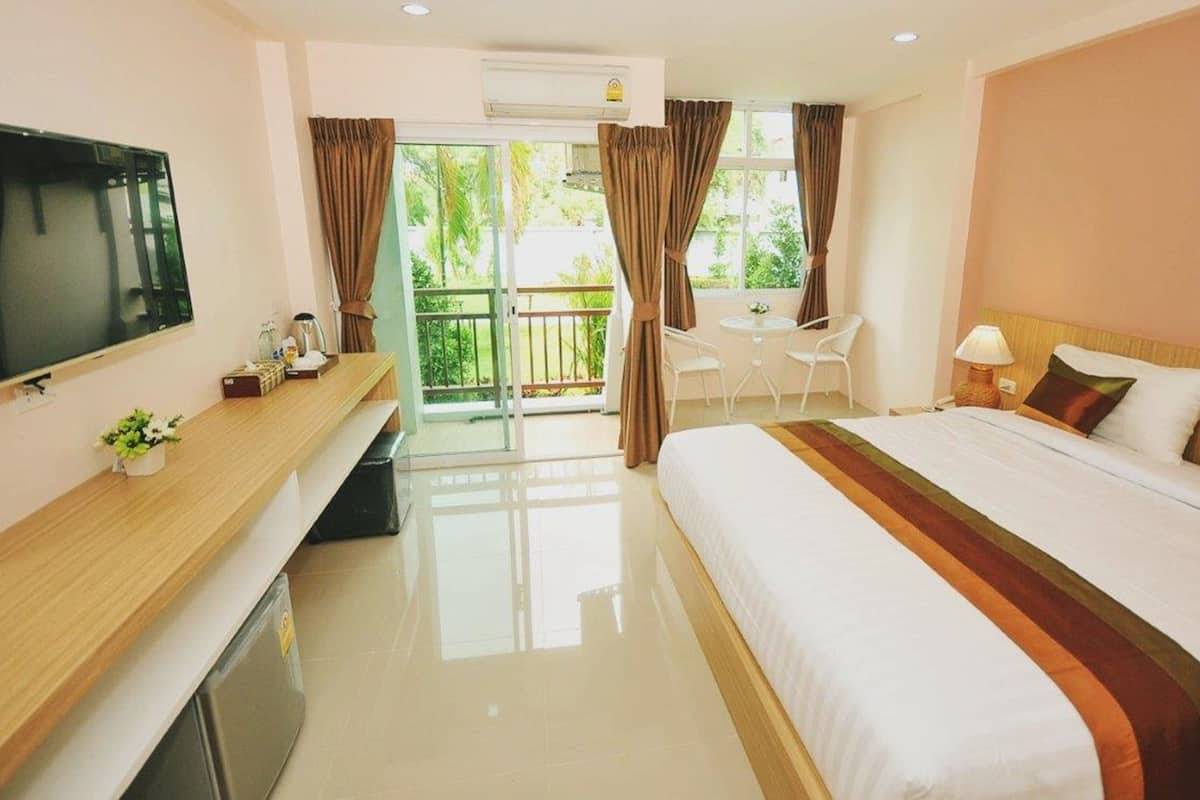 Quarto de hotel com cama, televisão, escrivaninha, cadeira e varanda com cortinas.