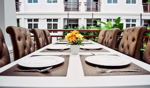 Mesa de comedor para seis personas con sillas tapizadas en marrón, mantel blanco y un jarrón con flores amarillas.