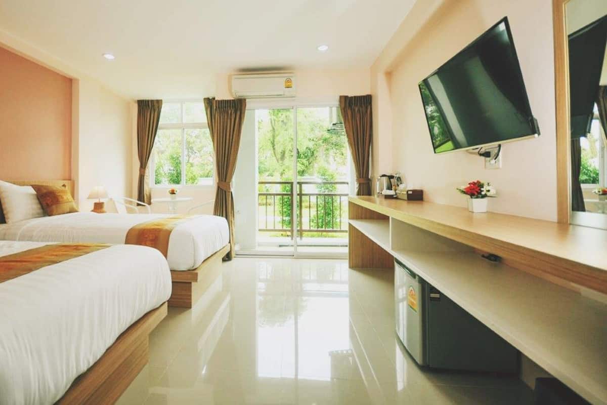 Quarto de hotel com duas camas, televisão, escrivaninha e varanda com vista para o verde.