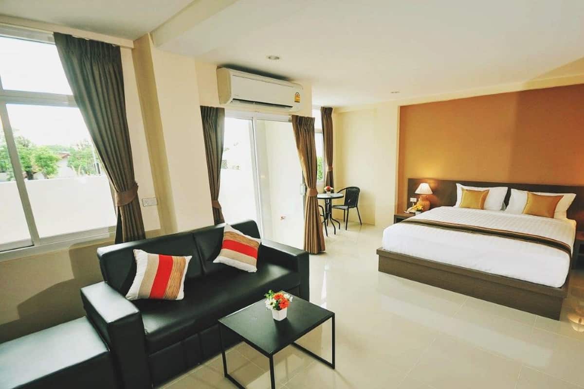 Quarto de hotel com cama, sofá, mesa pequena com flores, cadeira e janela com cortinas.