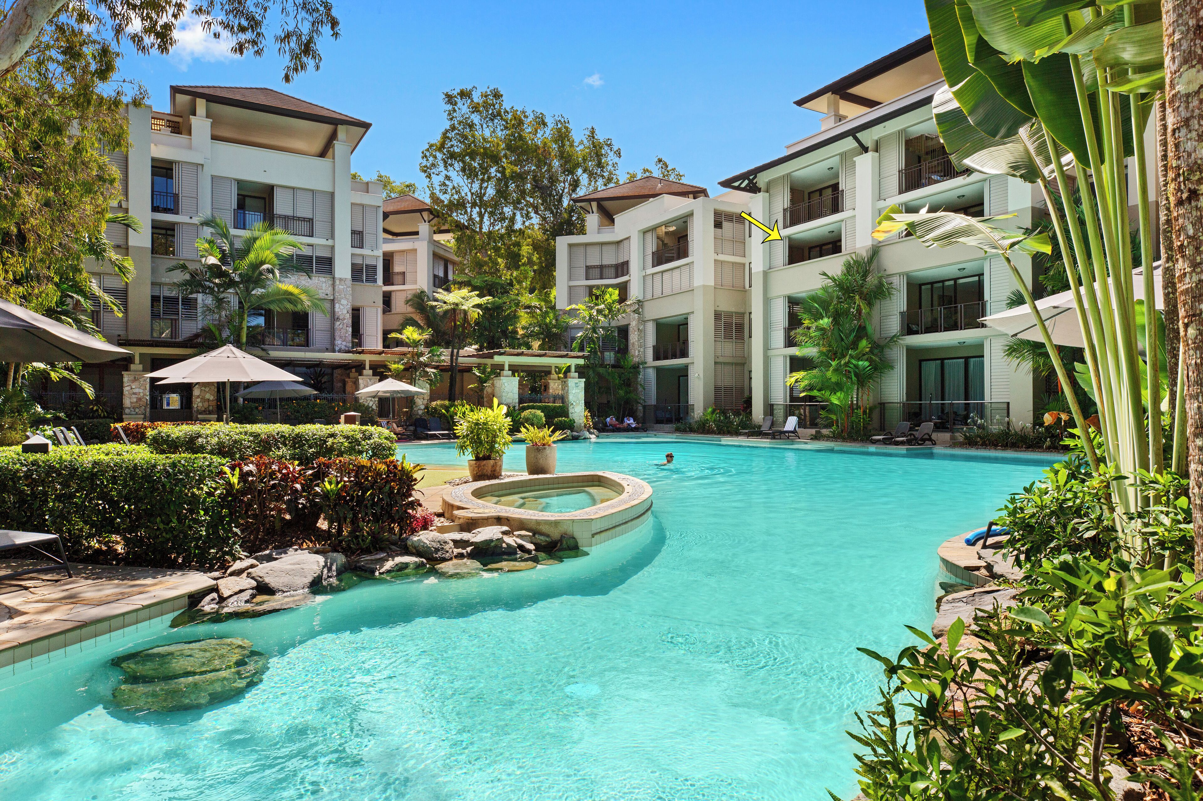 A resort pool area with multiple buildings, a hot tub, and lounge chairs.