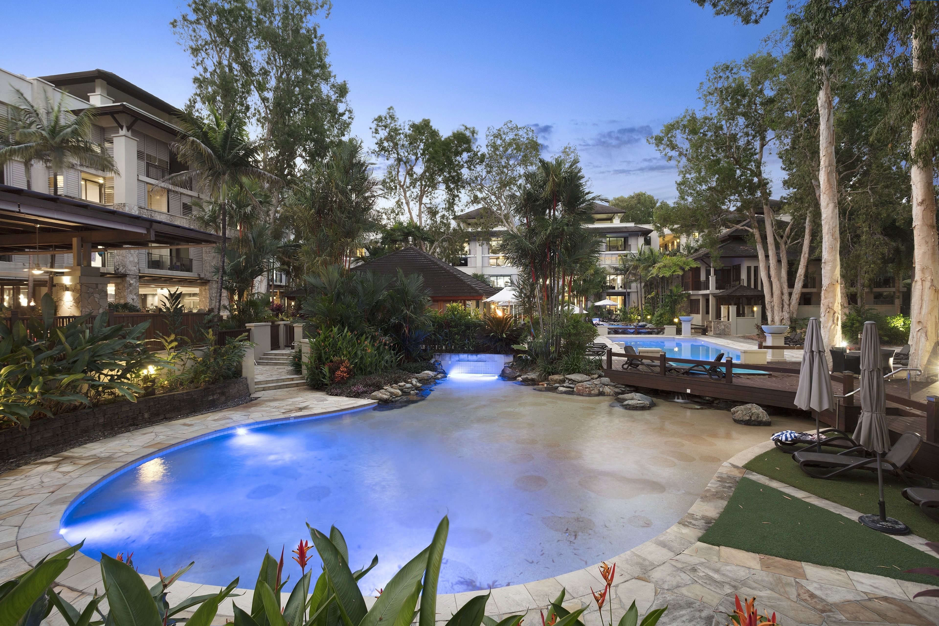 A resort pool area with a waterfall feature, surrounded by lush greenery and modern buildings.