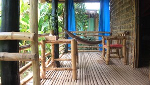 Una estructura de bambú con una hamaca, un banco de madera y techo de paja.