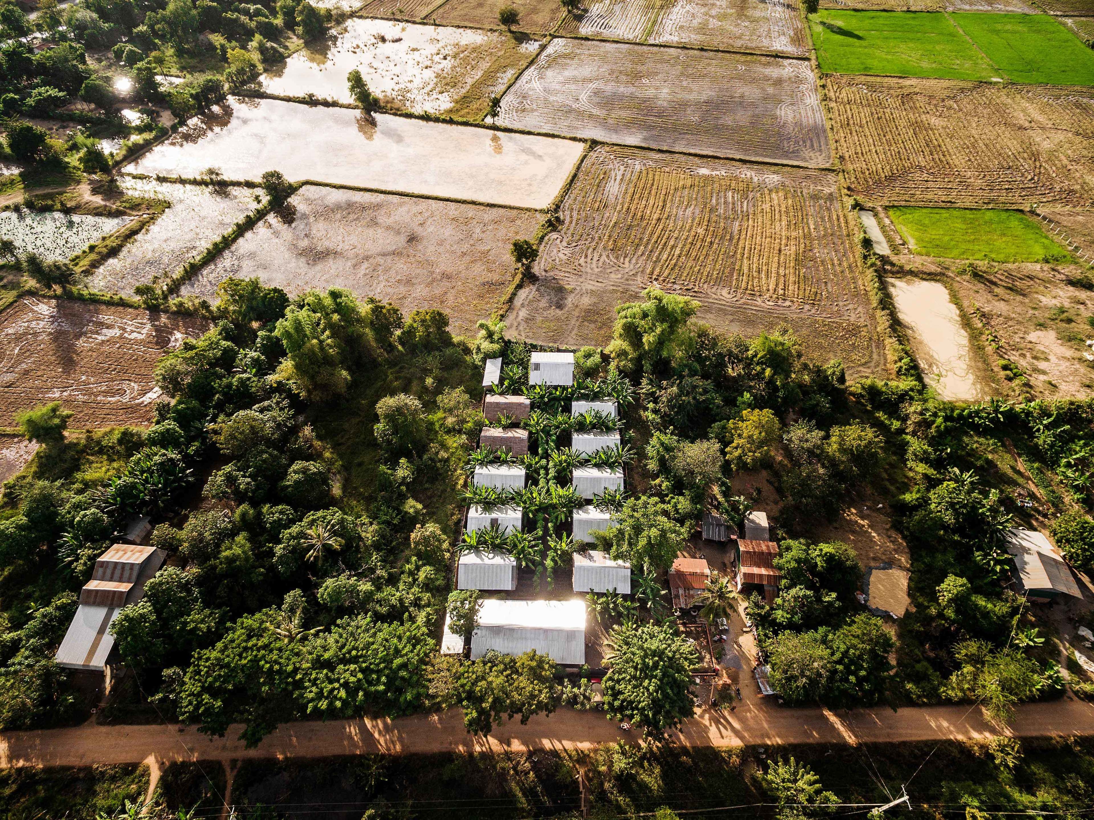Vista aérea de una zona rural con campos en terrazas, un conjunto de edificios blancos con paneles solares y un camino de tierra.