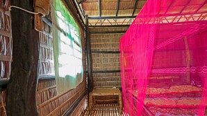 Una habitación con techo de paja, paredes de madera y una cama con mosquitero rosa.