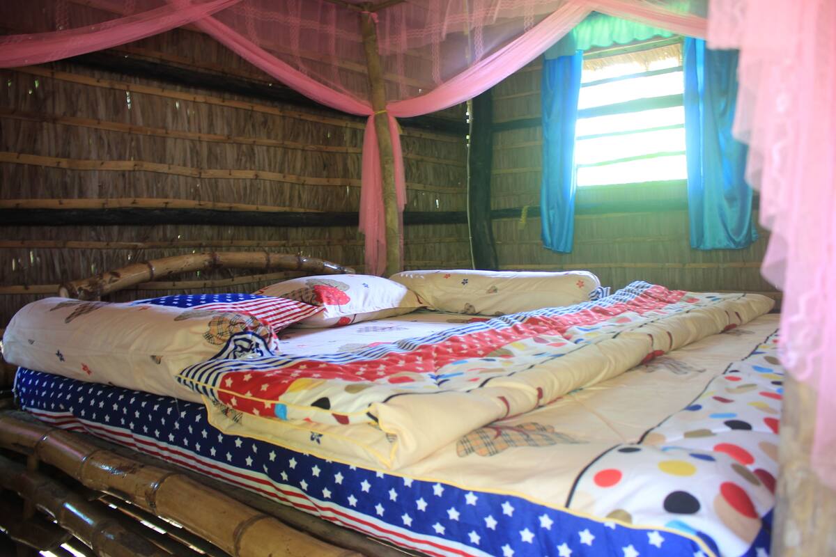 A bed with a quilt featuring stars and stripes, a canopy, and a window with blue curtains.