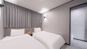 Una habitación de hotel moderna con dos camas, una mesita de noche, una lámpara de pared y una puerta corredera.
