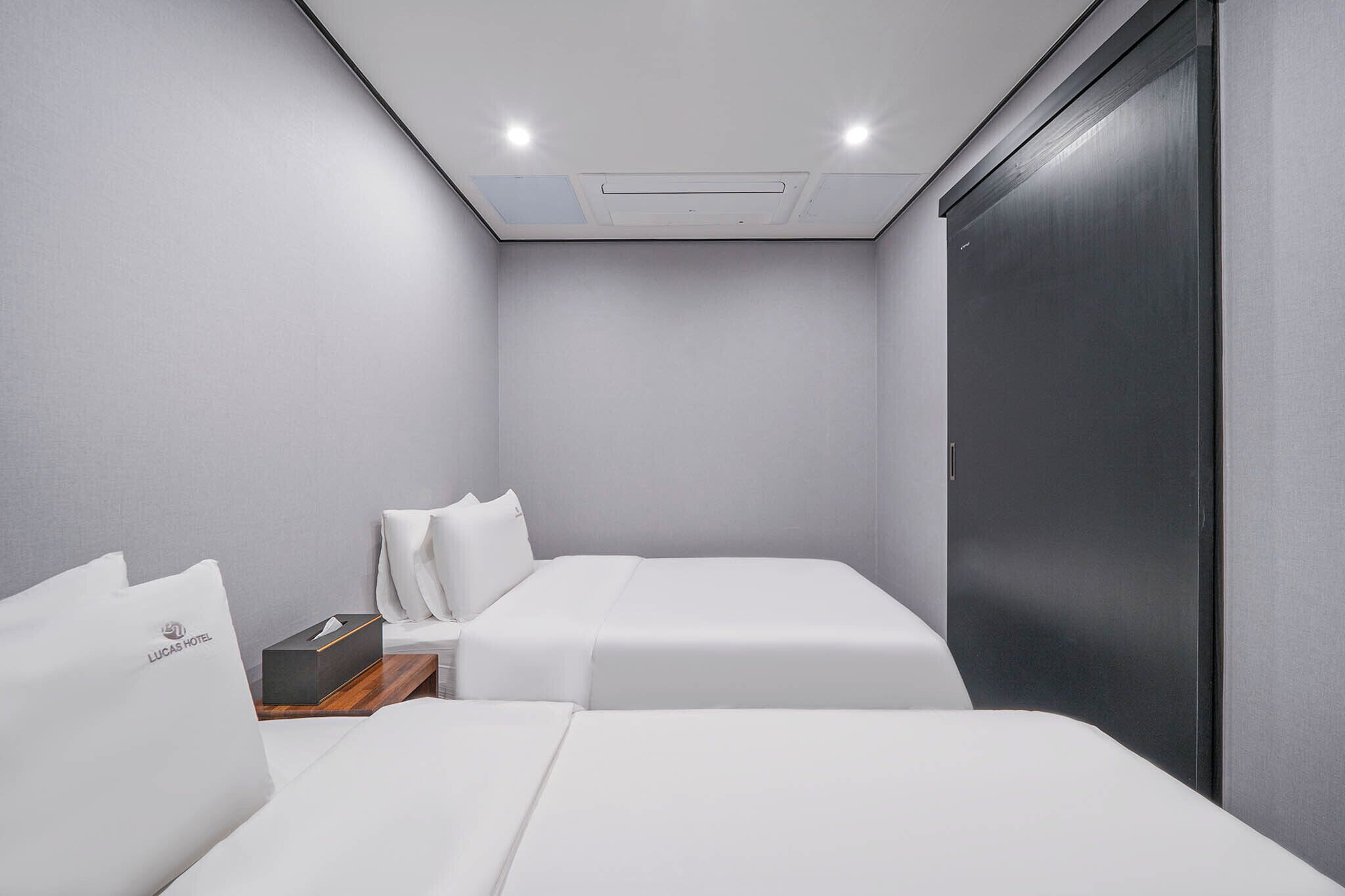 A modern hotel room with two beds, a wooden nightstand, and a dark door.