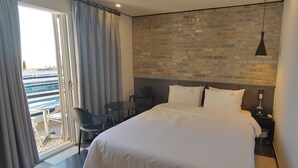 A hotel room with a large bed, a desk, and a chair. There is a brick wall behind the bed and a window with curtains. - Lucas Hotel (Changwon)