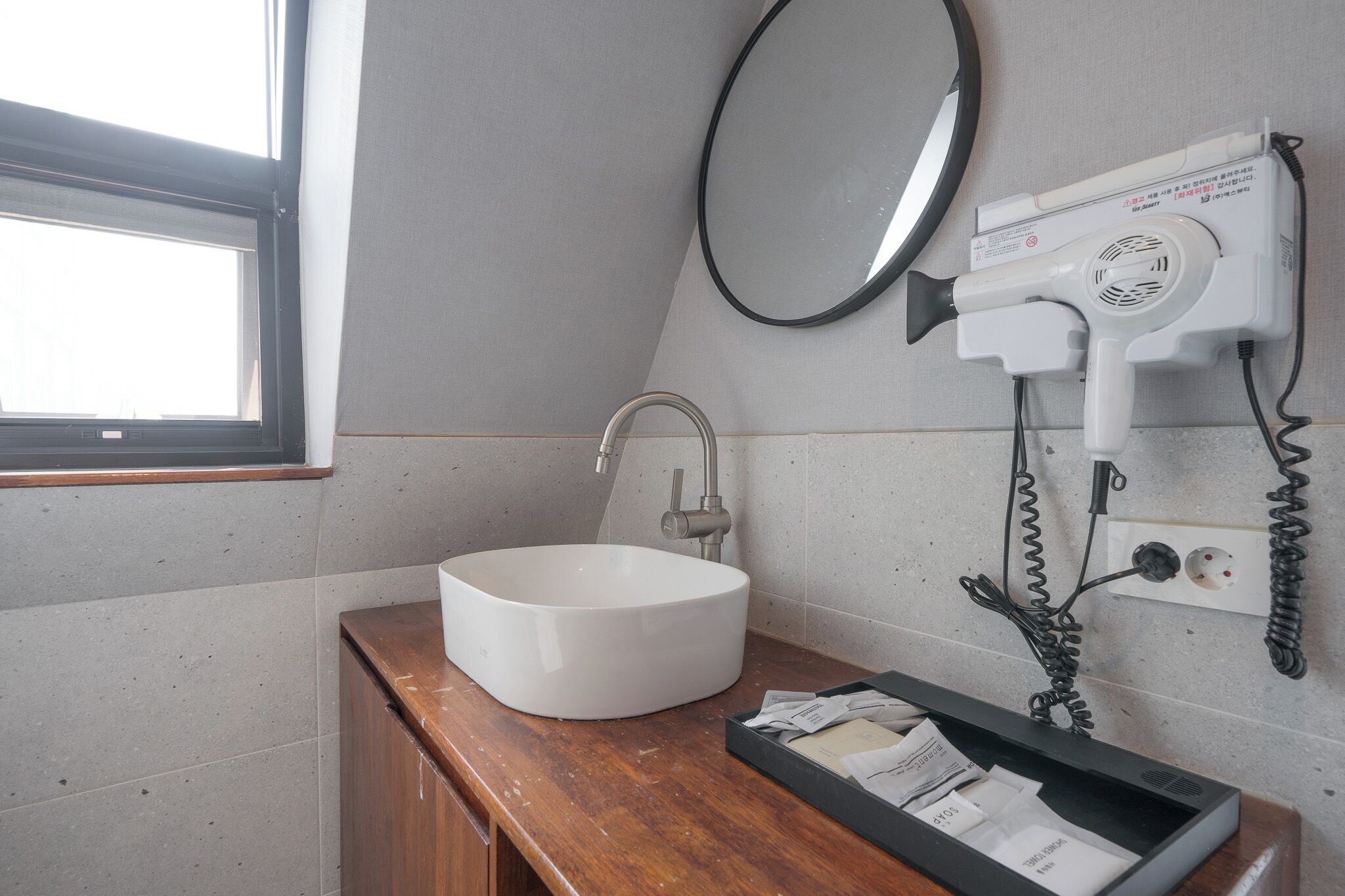 A bathroom with a white sink, a mirror, a hairdryer, and a window.