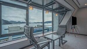 A modern room with large windows overlooking a body of water, two chairs, a table, and a tripod-mounted camera. - Lucas Hotel (Changwon)
