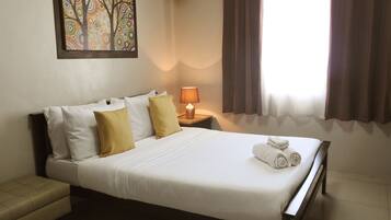 A neatly made bed with white and yellow pillows, a bedside lamp, and a framed artwork on the wall.