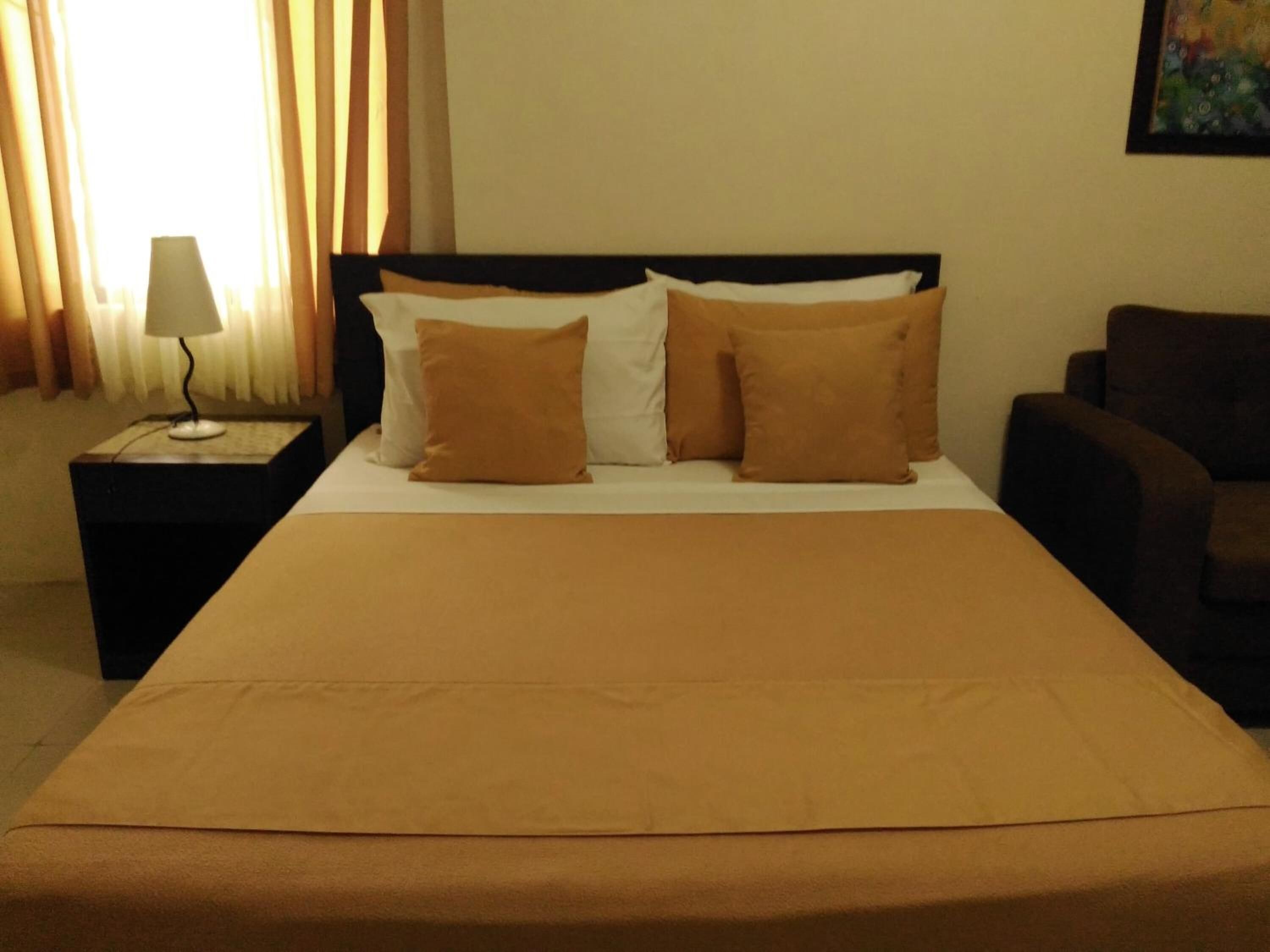 A hotel room with a bed, a nightstand with a lamp, and a chair.