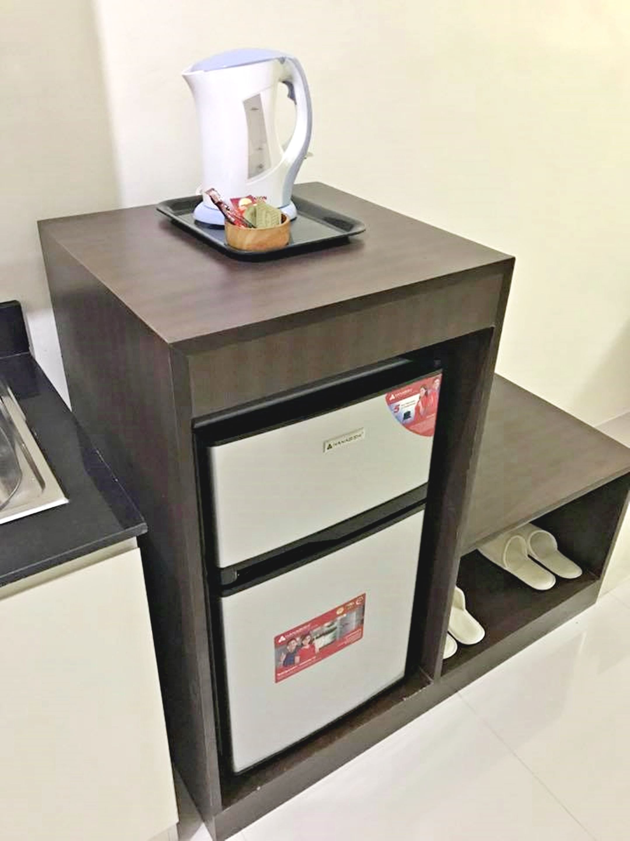 Minibar compacto com máquina de café, pequeno frigorífico e espaço para guardar sapatos.