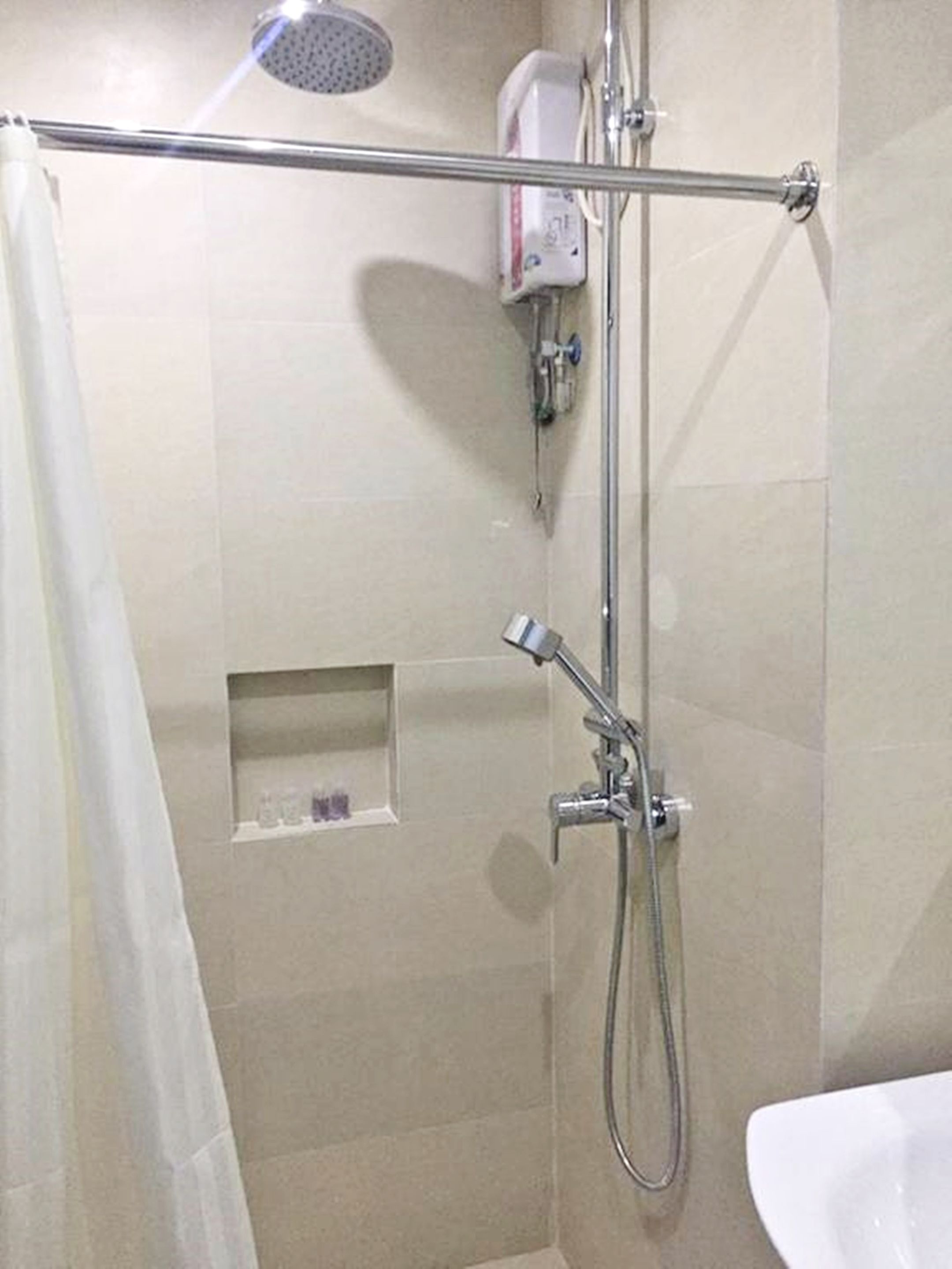 A shower area with a handheld showerhead, a wall-mounted faucet, and a soap dispenser.