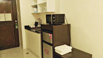 Una kitchenette compacta con microondas, estufa pequeña y pileta. Hay una toalla blanca sobre una mesada.