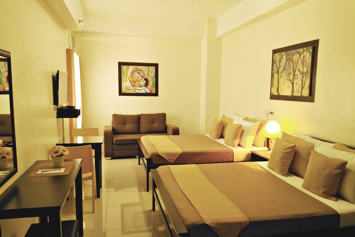 A hotel room with two beds, a sofa, a desk, and a lamp.
