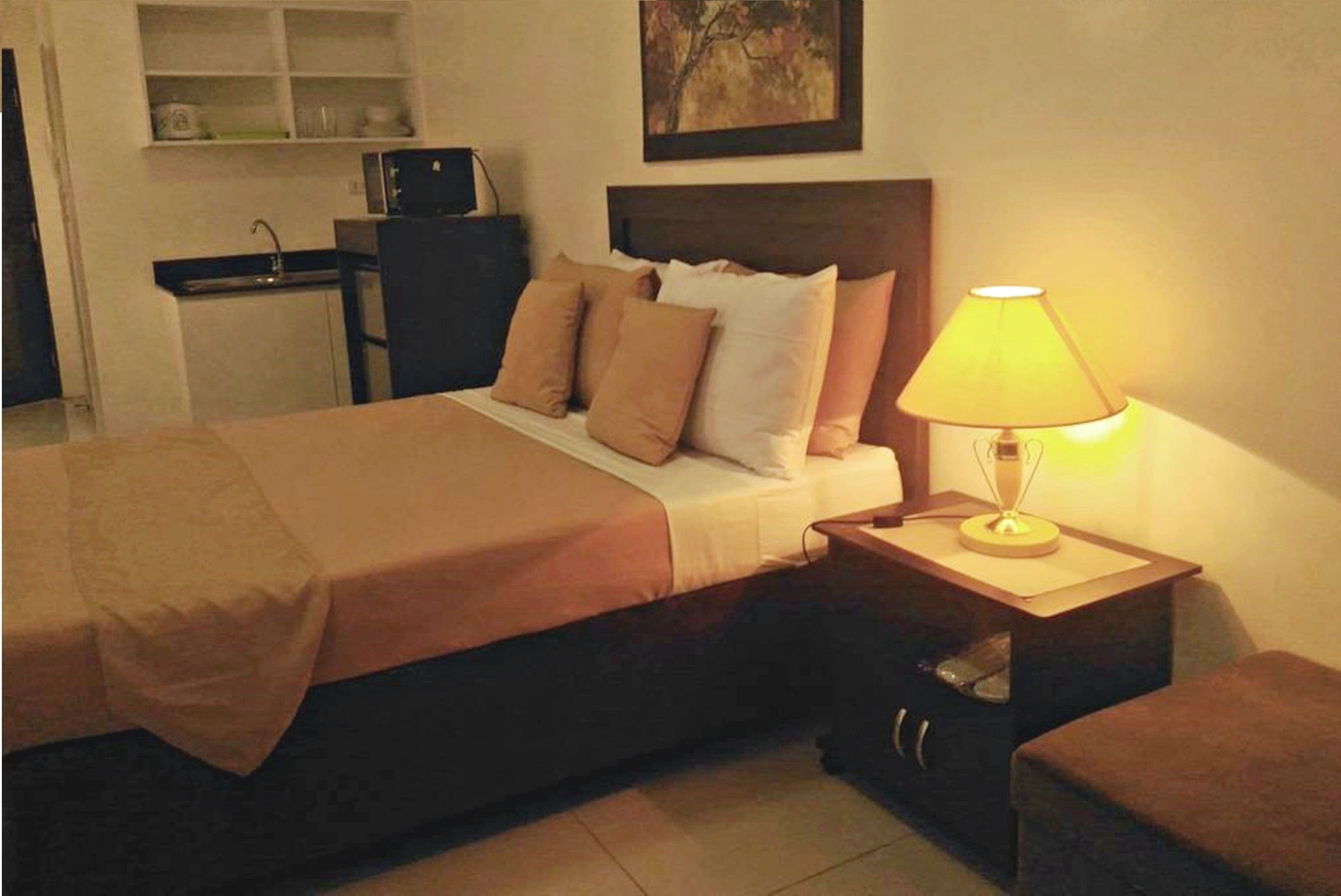 A neatly made bed with a brown bedspread, a bedside lamp, and a small wooden nightstand with drawers.