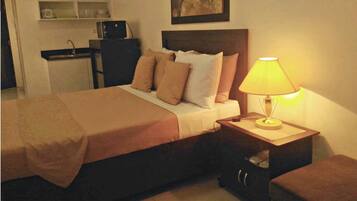 A neatly made bed with a brown bedspread, a bedside lamp, and a small wooden nightstand with drawers.