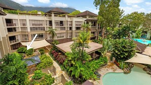 A hotel with multiple floors, outdoor swimming pool, lush greenery, and a mountainous backdrop.